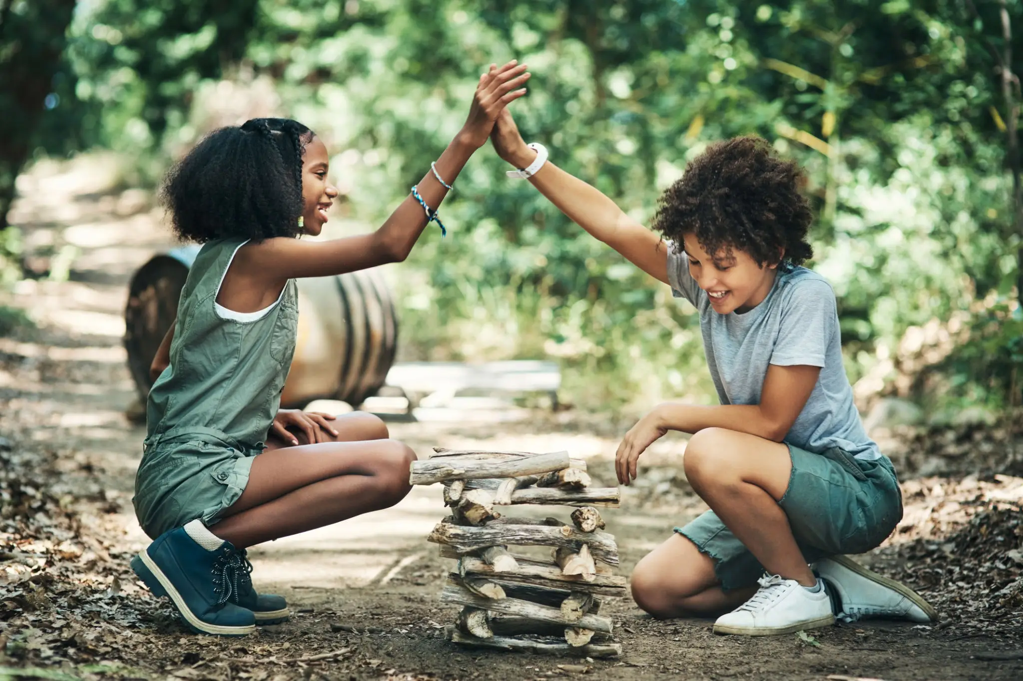 Children high-fiving beside stacked wooden sticks.