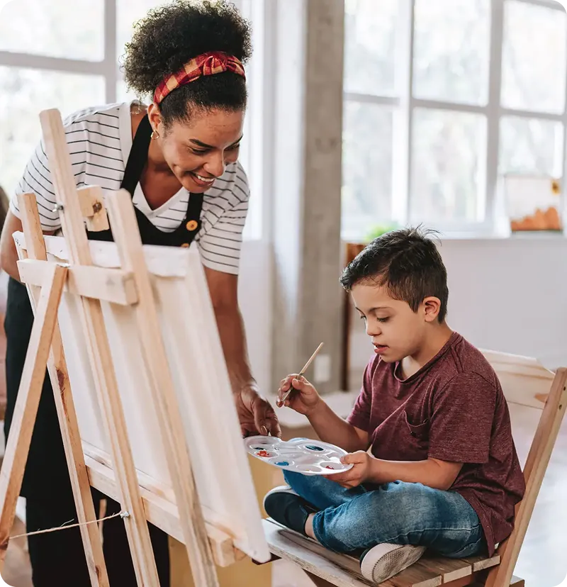Teacher assisting child with painting activity.