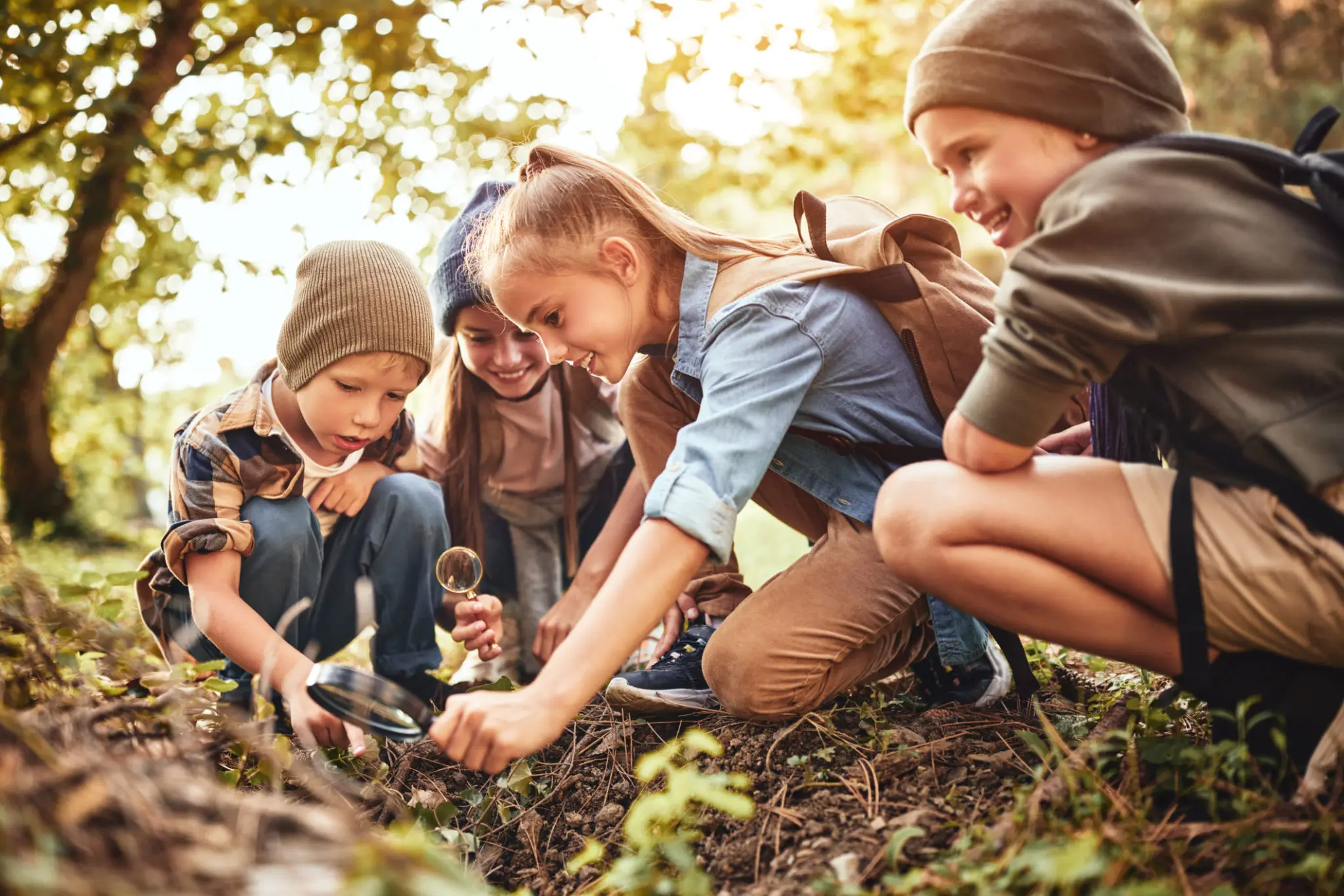 Children exploring nature with magnifying glasses outdoors.
