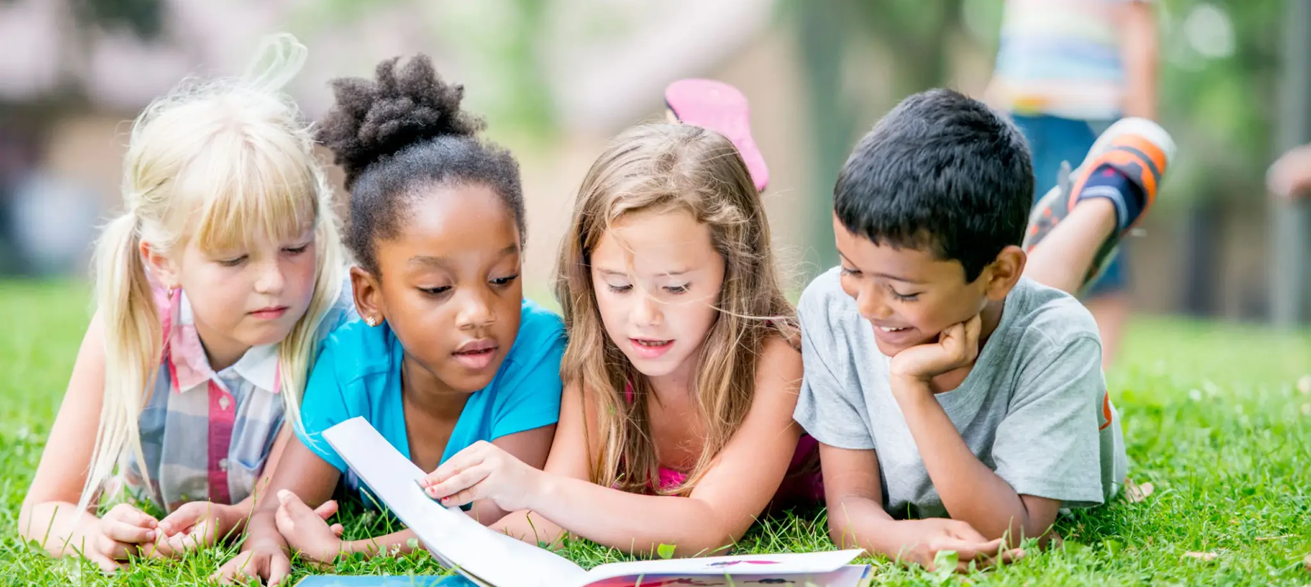 Children reading a book on grass.