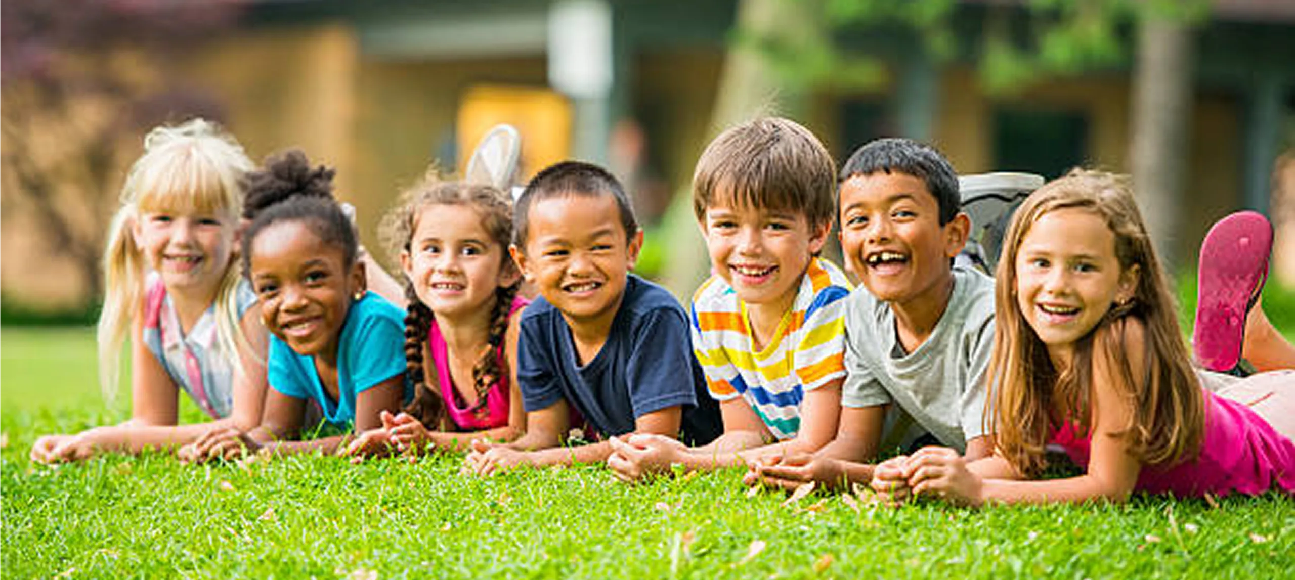 Smiling children lying on grass outdoors.