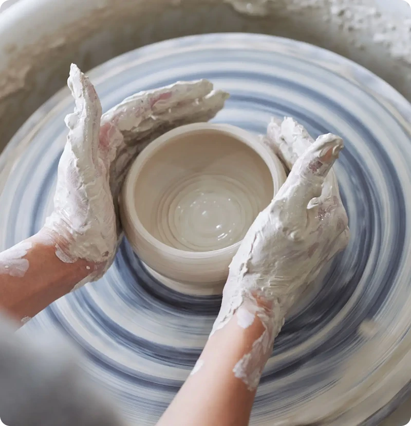 Hands shaping clay on pottery wheel.